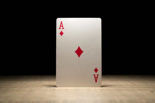 Brecht, Belgium - 29 may 2020: A portrait of the ace of diamonds standing up in the spotlight on a wooden table surrounded in darkness. There are no other playing cards of the deck in the picture.