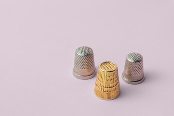 Triangular composition of three thimbles, two types, and one gold on a pink background. Sewing items.