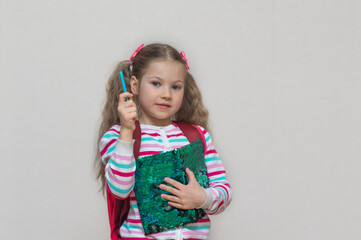 Back to school. Portrait of blonde schoolgirl with colored (shiny) notebook and pen in her hands. The girl is smiling and looking at camera. Thumbs up. Light gray background. Education. copy place.