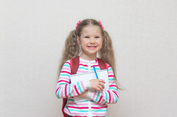 Back to school. Portrait of a blonde schoolgirl with a notebook and pen in her hands. She's surprised. Light grey Studio background. Education. Preparation for school. place to copy.