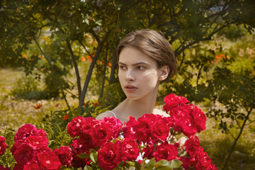 Naklejka premium Beautiful girl with spring blooming red rose flowers.
