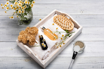 Glass bottles of essence or serum with chamomile flowers and roll up of white towels in a wooden...