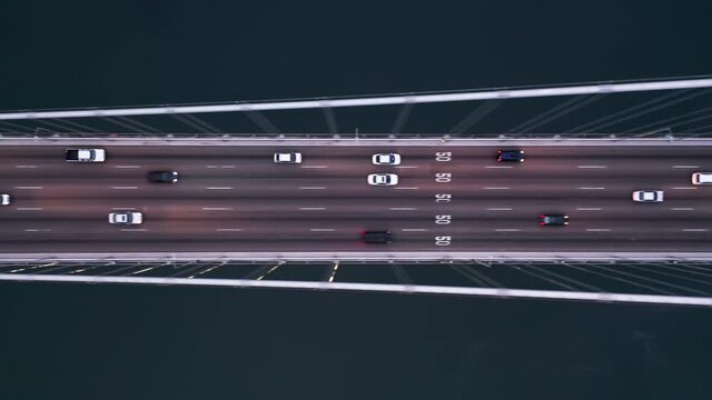 Cinematic industrial aerial of the contemporary architecture and engineering construction. 4K aerial top down over the traffic on the highway at night time. Cars are driving with head lights by bridge