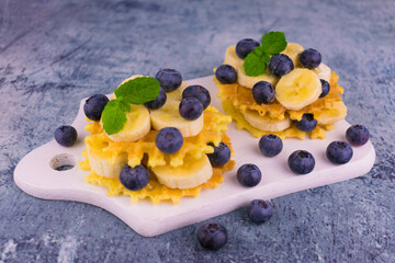 Waffles with blueberries and banana on a white board.
Delicious and healthy breakfast.