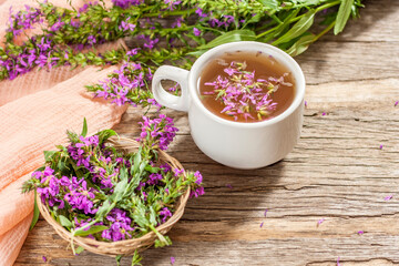 Obraz na płótnie Canvas Fireweed is a healthy herbal tea. Mug of traditional russian drink ivan tea on a wooden background with fireweed flowers