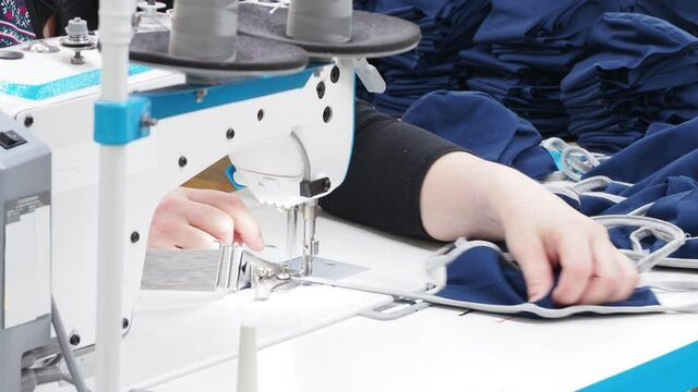 The process of covid-19 protective masks sewing on the overlock in the sewing shop. Close up of sewing process on the overlock in the sewing shop. Tailoring industry..