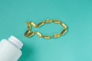 Fish oil capsules on green background. Capsules form the shape of a fish.