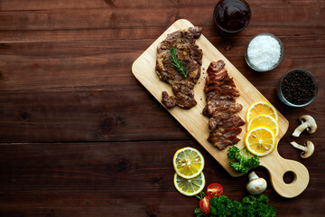 Top view of slide meat steak served with lemon and vegetable on wooden plate. Copy Space for Text.