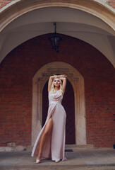 Fototapeta premium A girl in a chic long dress in full growth in the castle. Blonde model posing, woman with long legs. Summer on vacation in a historic city