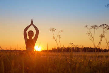young woman doing yoga at sunset in summer