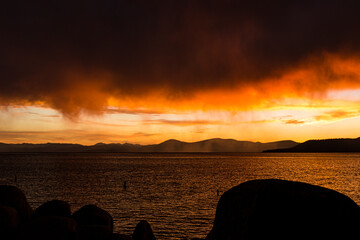 Brilliant orange sunset over Lake Tahoe with rocks and water in foreground