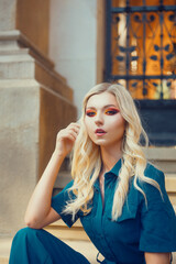 Fototapeta premium Blonde with beautiful smoky eyes makeup. Bright red shadows on a beautiful female face. A model on the street sits near the university in a suit. Fashion