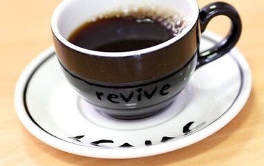 Black coffee cup with a white saucer with black writing,