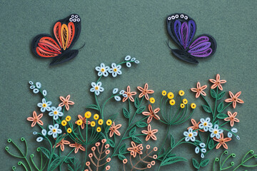 Butterflies, flowers and leaves isolated on a green paper background. Top view. Hand made of paper quilling technique.