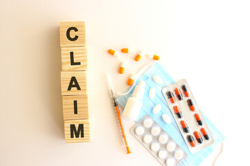 The words CLAIM is made of wooden cubes on a white background with medical drugs and medical mask. Medical concept.
