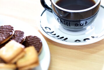 Black coffee cup with a white saucer with black writing and assorted biscuits,