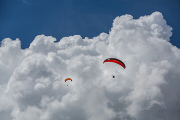 Roter und Oranger Gleitschirm mit Wolken. Gleitschirm Ohren angelegt.