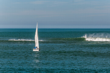 white sailboat in the sea with a big wave behind