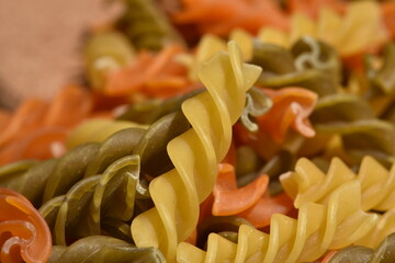 Composition of raw pasta uncooked tricolore fusilli, pasta twist shape. Close up and selective focus on colorful fusilli pasta.