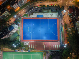 Aerial bird’s eye view of the outdoor hockey field at night. The image contains soft-focus, grain, and noise.