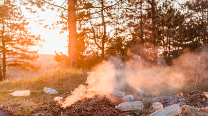 A stack of burning leaves next to a pile of bottles in the forest.