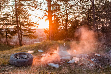 A car wheel next to a heap of burning junk in the forest.