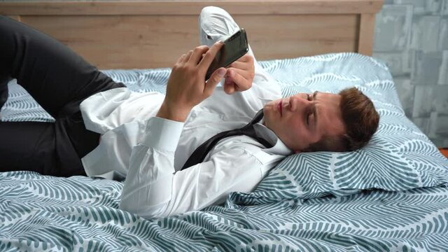 a man in a suit is lying on the bed using his phone