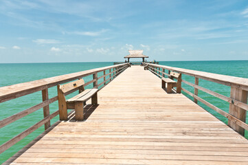 front view,  of a wood pier with benches, jutting out, one hundred yards, in the tropical waters of the gulf of Mexico, on a sunny morning
