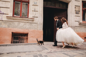 Happy newlywed couple hugging and kissing in old European town street, gorgeous bride in white...