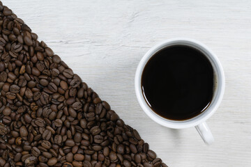Grains of coffee with a cup of coffee on a background of bleached wood.