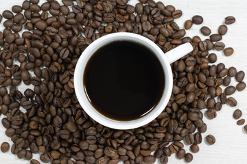 Grains of coffee with a cup of coffee on a background of bleached wood.