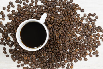 Grains of coffee with a cup of coffee on a background of bleached wood.