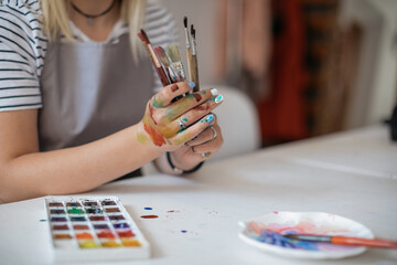 Close up of woman in apron holding painting brushes in art workshop. Copy space.