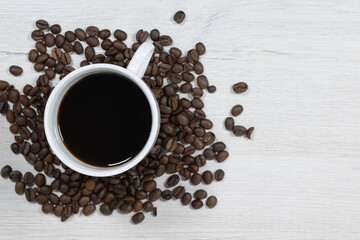 Grains of coffee with a cup of coffee on a background of bleached wood.