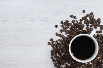 Grains of coffee with a cup of coffee on a background of bleached wood.