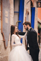Naklejka premium Wedding couple hugging in the old city. Blue vintage doors and cafe in ancient town on background. stylish bride in white long dress and groom in suit and bow tie. wedding day