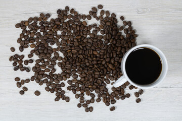 Grains of coffee with a cup of coffee on a background of bleached wood.