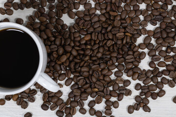 Grains of coffee with a cup of coffee on a background of bleached wood.