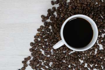 Grains of coffee with a cup of coffee on a background of bleached wood.