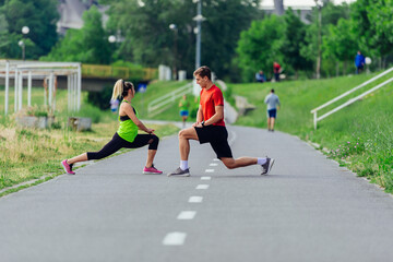 Fototapeta premium Young couple warming up and stretching together in a park before running