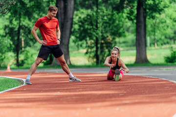 Young couple stretching before starting their morning jogging routine on a tartan track at the park.