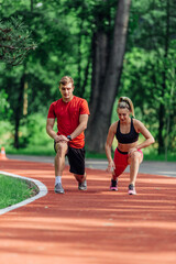 Fototapeta premium Young couple stretching before starting their morning jogging routine on a tartan track at the park.