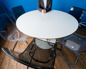 A faceless business woman in a suit sits alone at a round table in a meeting room. The female boss...