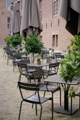 Outdoor tables and chairs with umbrellas and small potted trees. A restaurant or cafe on the street.