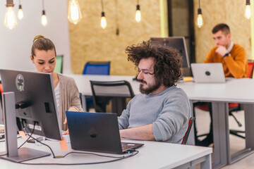 Two colleagues working on a project in modern startup offices. Guy with afro haircut and a female blonde employee working at the office.