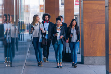 Full length of a group of colleagues in casual businesswear discussing business while walking at office hall.