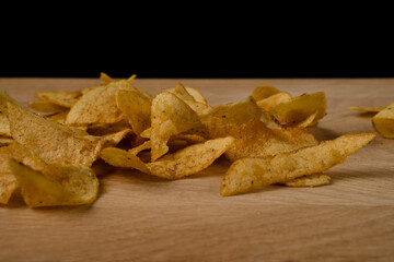 Appetizing potato chips are scattered on a wooden board