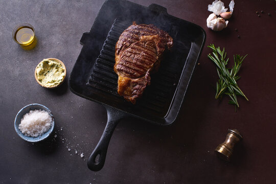 Cooked black angus prime beef ribeye steak on cast iron grilling pan with herbs, butter and spices