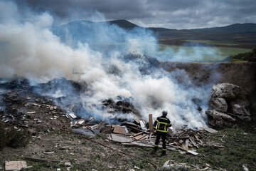 Back view of brave fireman in protective uniform standing with hose and extinguishing fire on dump in mountains