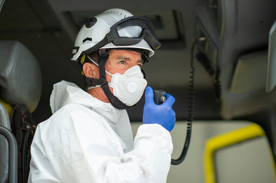 Side view firefighter wearing respirator and helmet sitting in fire car and using walkie talkie